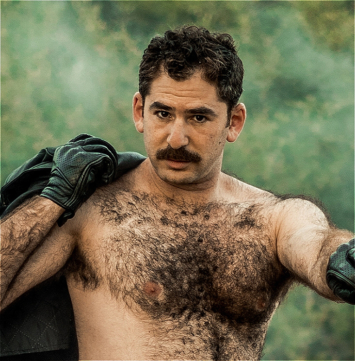 Josh is bare chested with black leather gloves and holds a black leather jacket over his shoulder