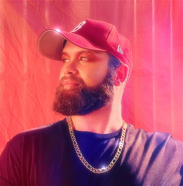 Photo of Garret Lyon with his head turned to the side wearing a red cap, black shirt and shining gold chain.