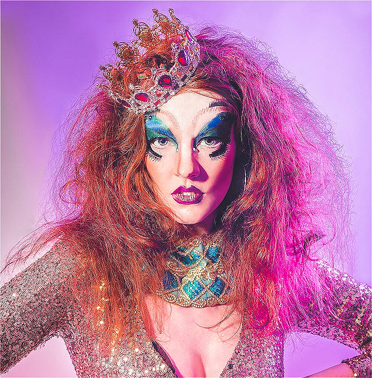 Woman in drag with wild hair pouts seductively against a pink background.