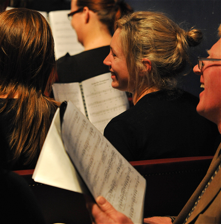 Two people singing holding sheet music and smiling.