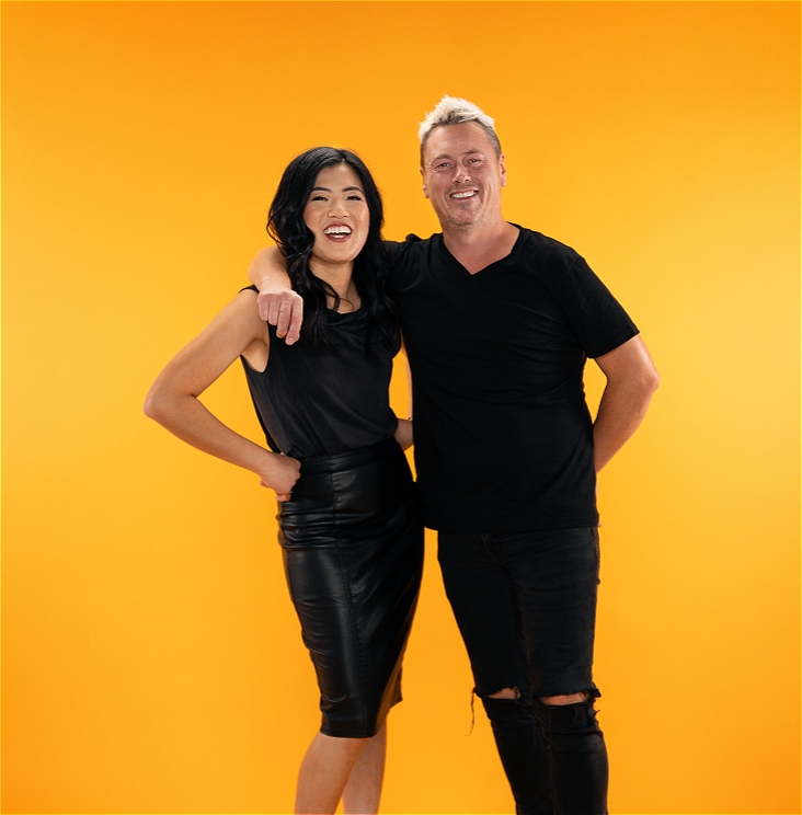 A woman and a man dressed in black standing in front of an orange background.
