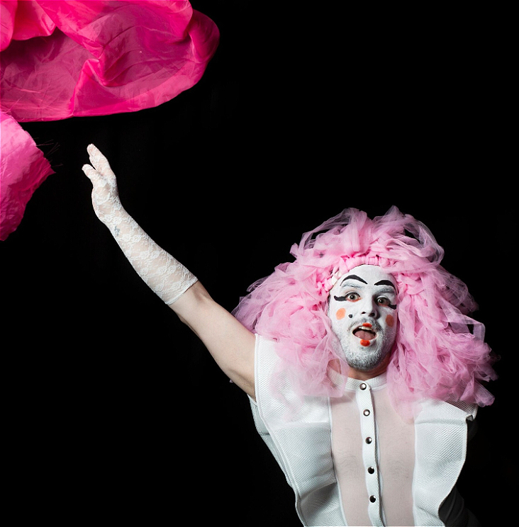 A person in white makeup and pink hair throwing a pink sheet