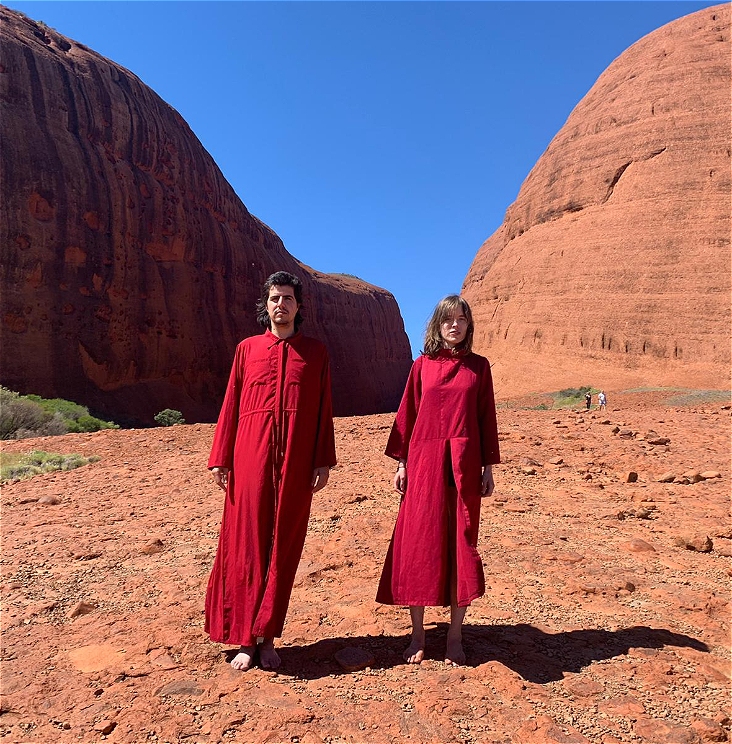 Two people dressed up in red robes and without shoes in a red landscape with a blue skye.