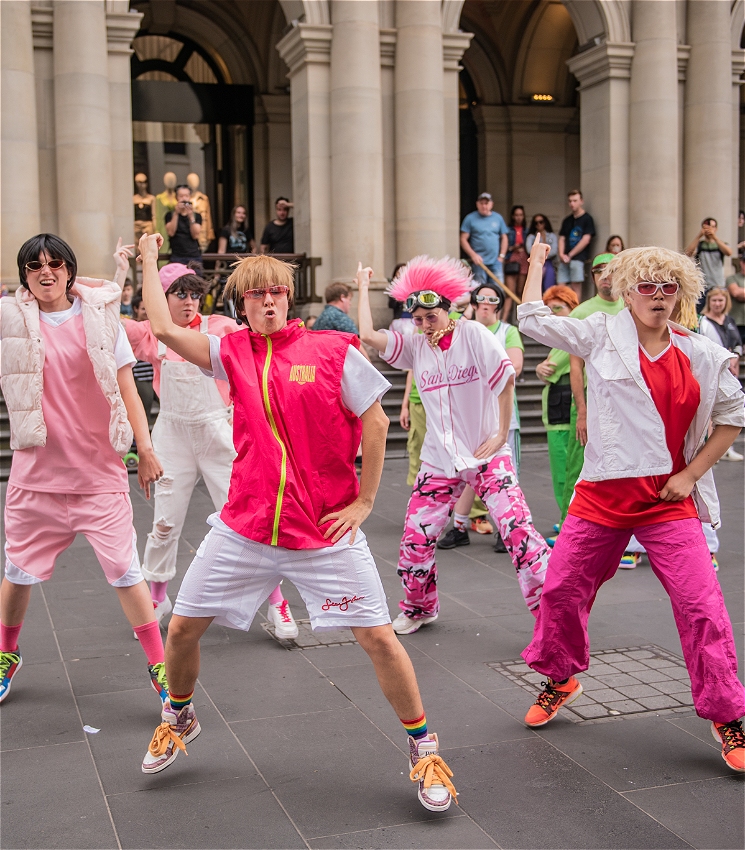 5 performers dressed in pink and white costumes dance together at Bourke St Mall. They are dressed like they are in a 90s boy band.