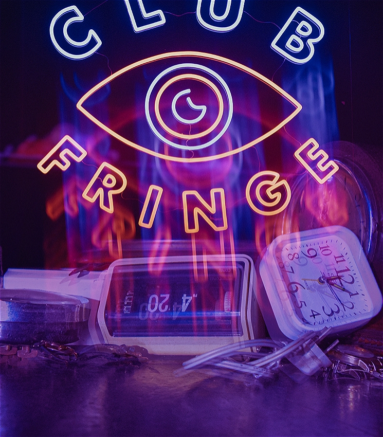 A hazy and artfully blurred image that shows several alarm clocks, some digital and some analogue, that are strewn across a surface. They all show different times. The image is overlayed with a neon logo which reads "CLUB FRINGE". In the middle of the two words is an the shape of an eye, with a crescent moon as the iris.