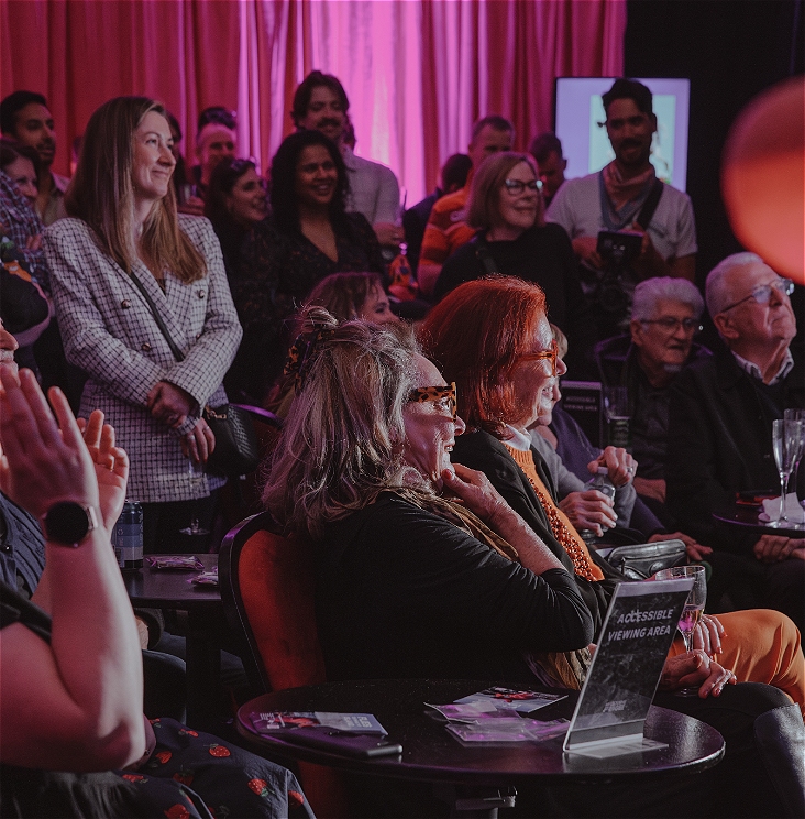 A group of people sitting in an audience, they are smiling and looking off to the right at something we can't see.