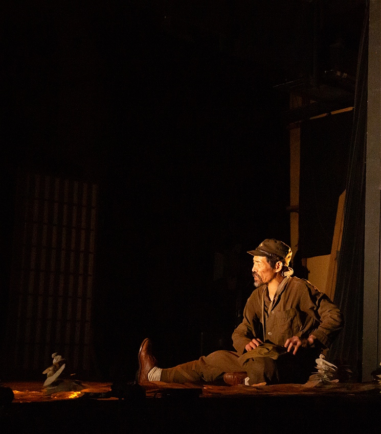 A tired Japanese WWII soldier sits on the ground in the right of the image, looking to his left.