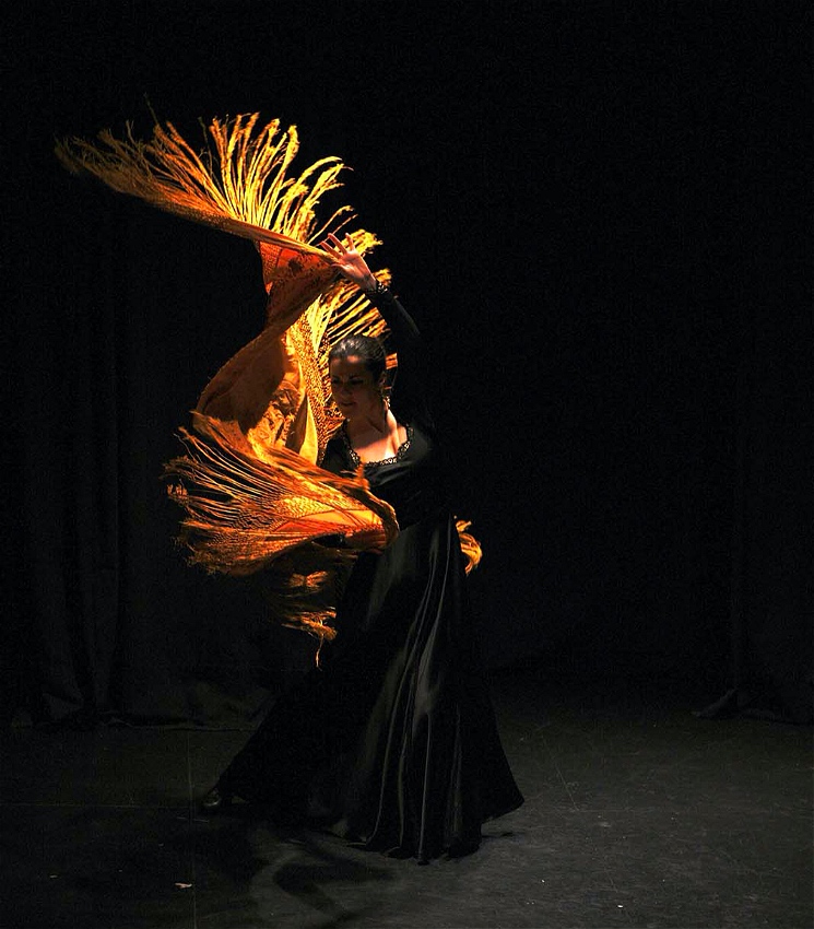 A flameco dancer dances wuht a golden shawl.