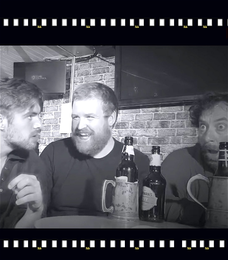 Three men sit in a pub, their drinks on the table in front of them.