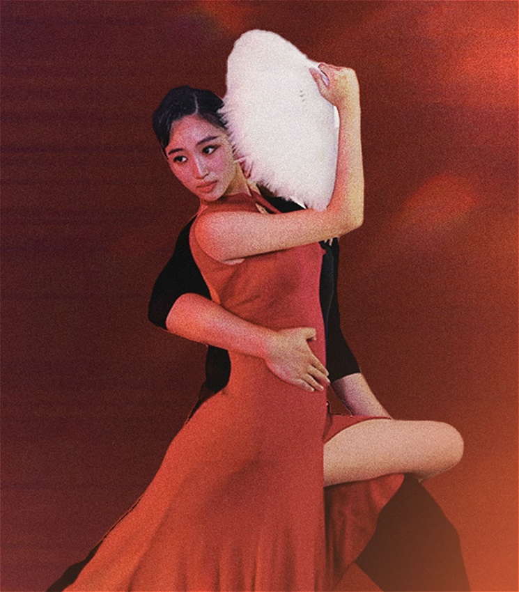 A man and a woman dance. The woman is in a red dress and covers the man from view. The man wears black. A white fan covers the man's face.