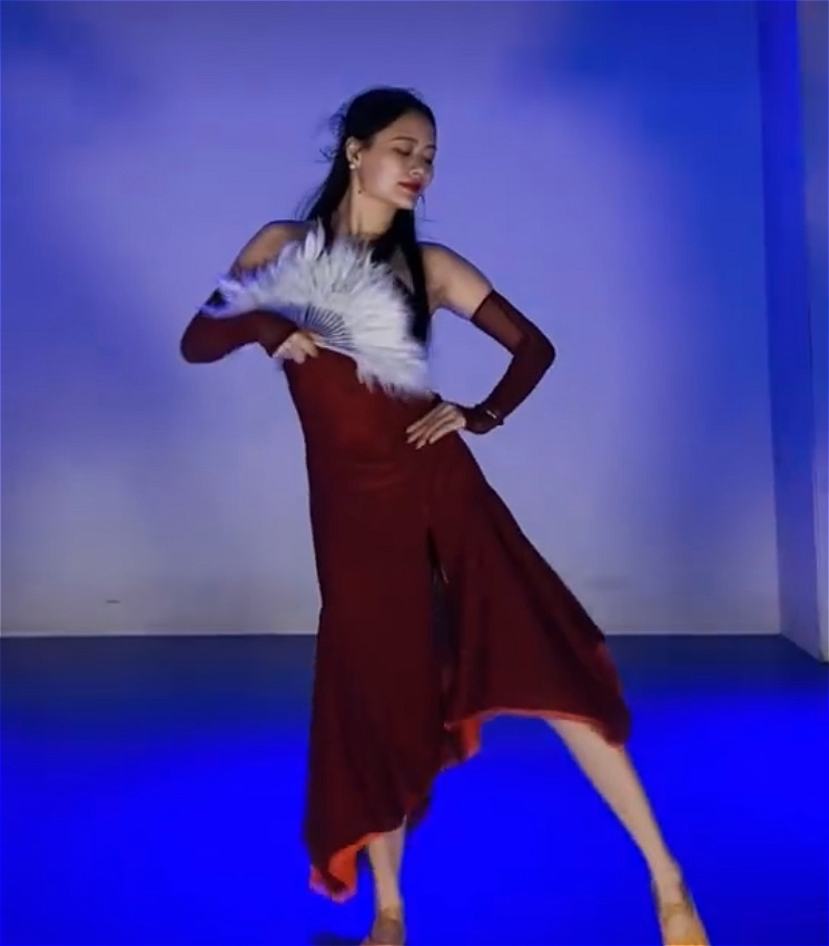A woman in a red dress holding a white fan dances on a blue floor.