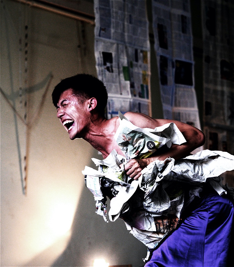 A figure partially covered in newspaper appears to be screaming or laughing. More newspapers line the wall.