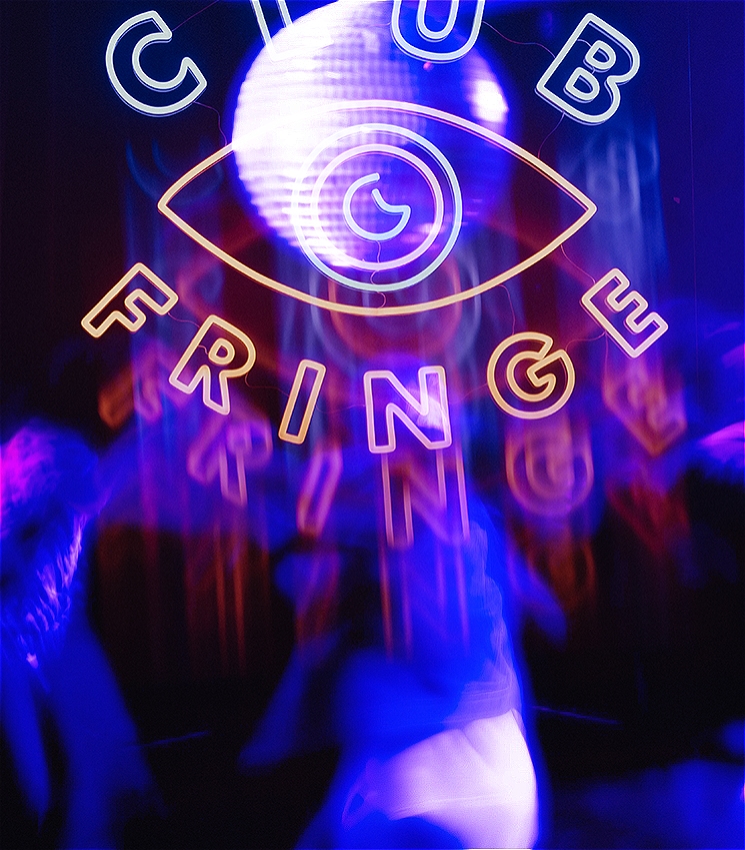 A hazy and artfully blurred image of a group of people dancing energetically around each other. There is a shining disco ball, amongst deep blue, pink and purple lights in dark room. The atmosphere is reminiscent of a club night. The image is overlayed with a neon logo which reads: CLUB FRINGE. In the middle of the two words is an the shape of an eye, with a crescent moon as the iris.