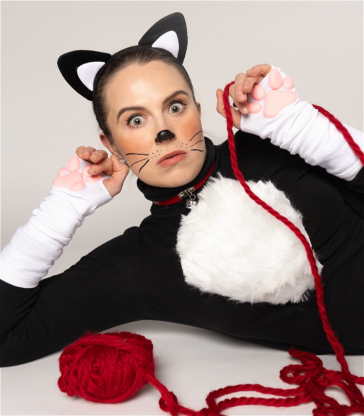 A woman wears a cat costume and plays with a ball of red yarn, she looks at the viewer wide eyed with her hands up like paws