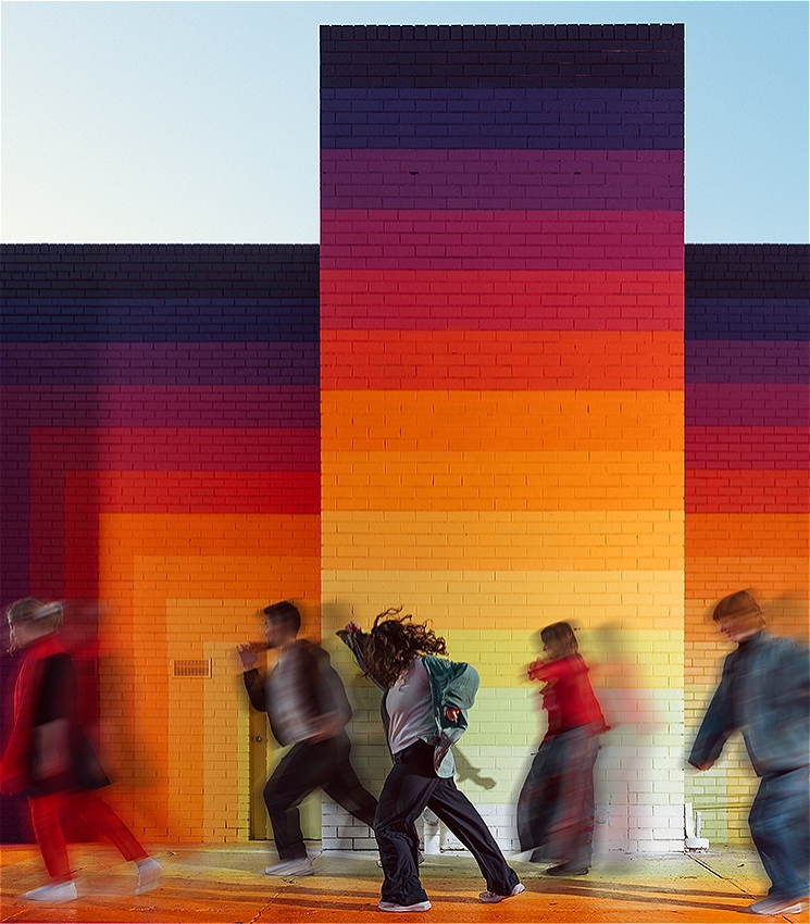 There are five people moving in front of a brightly coloured painted rainbow mural by Drez. The people are blurred in motion.