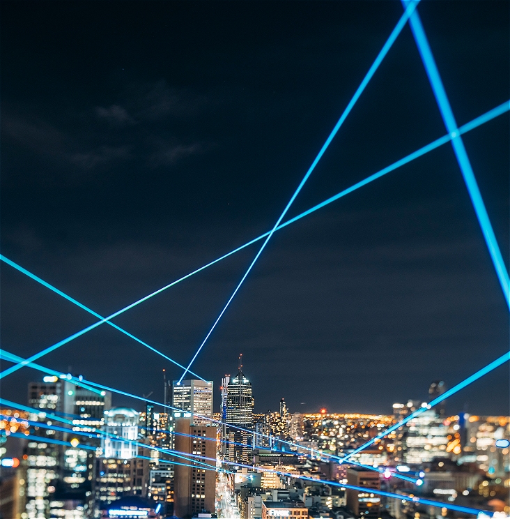 An image of the Melbourne cityscape lit up at night. There are various blue lasers pointing in different directions through the sky.