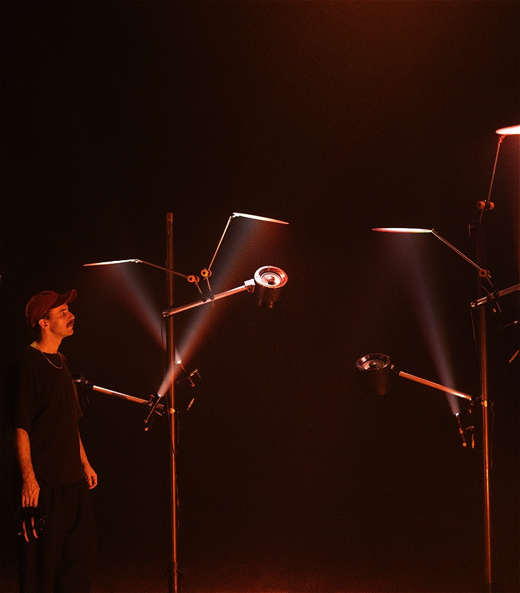 Artist standing in a forest of speakers, red light shining through