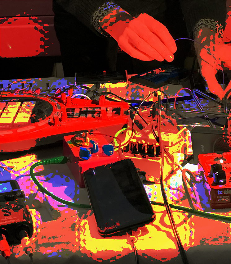 Closeup image of electronic music equipment with hands hovering over it, pixelated with bright colours.