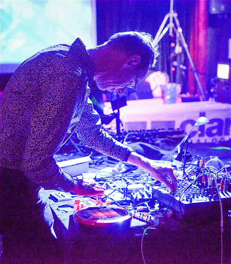 Nick Wilson adjusting parameters on electronic music equipment on a table in a darkened venue.