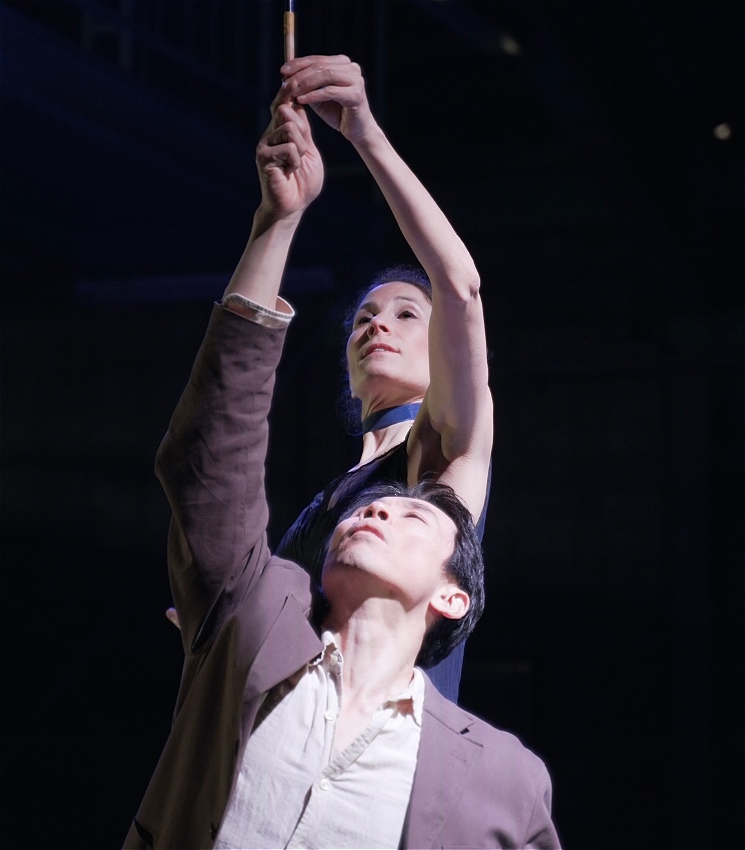 A man and a woman hold a stick above their heads.