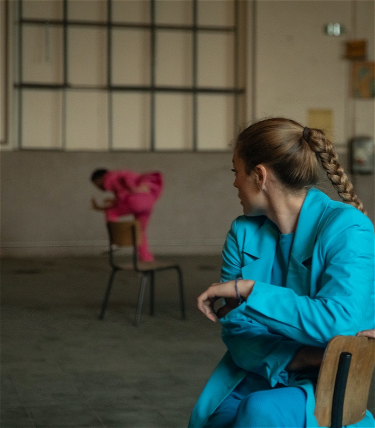 A woman in a blue dress looks at a person in pink dancing.
