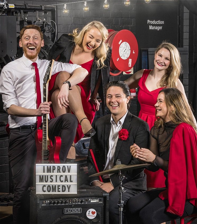 5 performers in various states of joy dressed smartly in red and black around musical instruments.